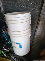 Two stacked white plastic buckets with dirt marks and a partially torn label on one bucket.