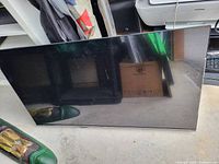 Photo of a 32 inch flat screen television with black frame, showing the TV face downward on a concrete floor with some reflections and smudges.