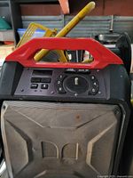 Front view of portable speaker showing control buttons, USB port, AUX input, circular dial with numbers, and front speaker grille with wear and dirt.