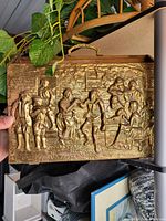 Top view showing raised brass relief of people engaged in outdoor activities including playing music and archery.