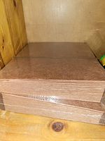 Photo shows three thick stacks of brown file folders, shrink-wrapped together, placed on a wooden surface against a wall.