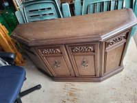 Angular wooden hall stand cabinet with carved floral details and metal handles seen from the front on a floor