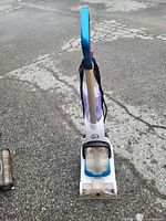 Front view of a white and blue upright Hoover vacuum cleaner with clear dirt container and black power cord wrapped around the handle.