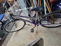 Full side view of purple Huffy mountain bike leaning against wall with garage tools in background