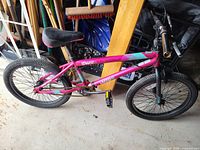 Kids BMX bike with pink and black frame, black seat, and black tires inside a garage environment.