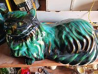 Photo of a large ceramic cat statue with green and black glaze placed on a shelf.