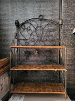 Photo shows a three-tier shelving unit made of dark metal frame with woven wicker shelves and decorative butterfly pattern on back.