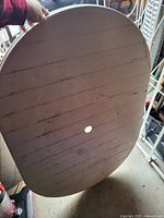 Wooden oval shaped patio table top with a hole in the center for umbrella placement, showing surface grain and some wear marks.