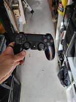 Black PS4 DualShock controller held in hand showing standard layout and touchpad, visible wear from usage