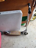 Razor kick scooter leaning against a table, showing full side profile with wooden deck and aluminum frame.