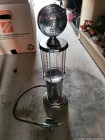 Silver gas pump replica with hose laid horizontally on floor, showing overall item details including top branding and nozzle