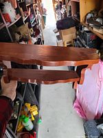 Handheld view of two-tier wooden wall shelf showing natural wood finish and curved edges.