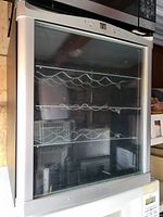 Front view of the silver wine fridge showing the glass door and metal racks inside