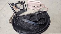 Photo showing all three handbags together: clear bag with black piping and chain strap, black embossed quilted semi-circular bag, and pale pink structured handbag.