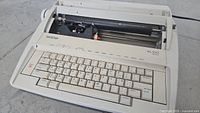 Front and top view of beige Brother ML100 electric typewriter showing keyboard and platen area with visible dirt and dust.