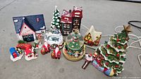 All the Christmas-themed ceramic figurines and houses included in the lot arranged on the floor showing variety and details.