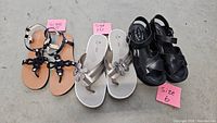 Three pairs of sandals side by side on gray surface with size markers: size 7.5 black Calvin Klein, size 10 silver Kork-Ease, size 6 black Clarks.