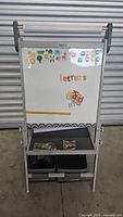 Full view of children’s easel with magnetic whiteboard showing magnetic letters, animal magnets, and storage bins with art supplies underneath.