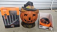 Photo of three items: box of LED icicle string lights with green bulbs and spider web design, ceramic or resin pumpkin decoration with a carved face and cat silhouettes, and Star Wars Mandalorian shadow projector light in orange and black with Grogu.