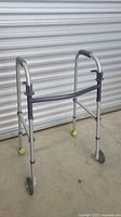 Full view of height adjustable silver aluminum walker with two front wheels and tennis ball covers on rear legs