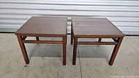 Pair of mid-century modern wooden side tables with brown finish placed on concrete floor.
