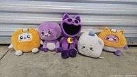 Five plush toys from Lankybox and Poppy Playtime lined up on concrete