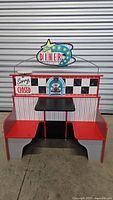 Front view of the double-sided play diner set with booth seating showing red and black seats, black table, checkered and striped design, 'Star Diner' hanging sign, and 'Sorry We're Closed' sign.