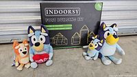 Fort building kit box with four Bluey plush toys arranged in front, showing various sizes and colors of plush toys and the packaged kit.