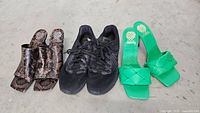 Three pairs of size 9.5 women's shoes on concrete floor: black Nike sneakers, brown snake print heeled mules, and green heeled sandals.