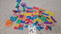 Various multicolor translucent plastic marble run pieces and marbles laid out on floor with Idea Booklet at center