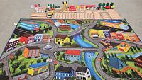 Complete view of wooden train tracks, train cars, and accessories arranged at the top of the fabric play mat showing city and road details.