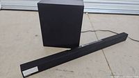 Soundbar with subwoofer behind it, showing the black color and rectangular shapes of both items.