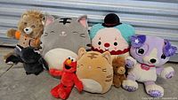 Full collection of 8 plush toys on concrete floor including Squishmallows, Elmo, Teddy Ruxpin, clown, dog, horse, and bat.