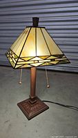 Full view of Tiffany style stained glass lamp with cream and amber shade, dark brown textured base, two pull chains visible.