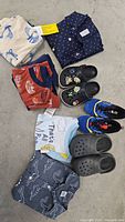 Overview photo of toddler boy's clothing and shoes displayed on the floor, including shirts, sleepwear, sneakers, and Crocs.