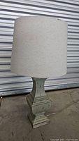 Full view of the vintage table lamp with beige drum shade and distressed green wooden base.