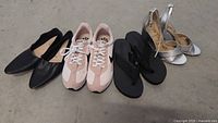Four pairs of women's shoes in size 10 arranged on the floor: black Sam Edelman flats, pastel pink and white Nike sneakers, black a.n.a flip flops, and silver Oleyo heels.