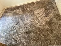 Overall view of taupe microfiber shag area rug with geometric pattern laid on carpeted floor, showing texture and color.