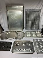 Various metal baking pans, tart pans, shaped cookie sheets, muffin pan, and cooling racks arranged on table.