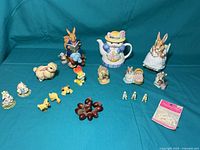Overview of entire collection showing Rabbit music box, ceramic rabbit teapot, multiple small animal figurines including ducks, rabbits, lambs, and mice, plus decorative miniature apples and small packaged accessories.