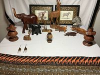 Overview of all carved wooden figurines, brass giraffes, candlesticks, and framed animal prints on a white surface with patterned cloth at front.