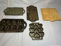 Five shaped pans on flat surface showing details: house, numbers and tools, animal shapes, hearts, and train shapes.