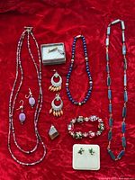 Full overview of the costume jewelry lot on red background showing all items including necklaces, earrings, bracelet, and pendant.