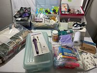 Overview showing a large collection of assorted craft supplies including dyes, threads, glue, iron-on patches, rhinestones, and tools arranged on a table.