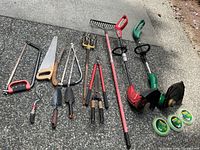 Photo showing all garden hand tools, saws, and small rakes arranged on concrete surface.