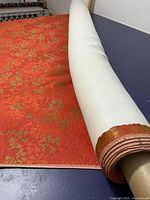 Close-up of the large roll of vibrant orange upholstery fabric with golden floral patterns, partially unrolled