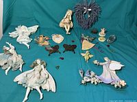 Overview of assorted fairy decor showing multiple white resin fairy figurines, metal enameled hangings, and floral pieces.