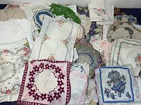 Overview of assorted vintage handkerchiefs and crocheted doilies with embroidered, printed patterns and lace trims, laid out for display.