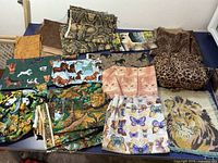 Wide view showing multiple pieces of quilting fabric with various animal prints including cats, butterflies, lions, jungle animals, horses, and leopard print.