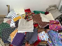 Multiple pieces of quilting fabric laid out in a pile showing various colors and patterns including solids, florals, geometric and novelty prints.